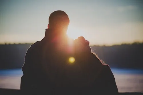 Two people standing together silhouetted against sunset over water